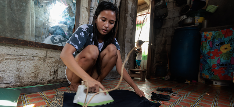 Ronita ironing clothing in her home in the Philippines. Photo: Richard Wainwright/Caritas Australia
