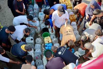 People fill containers from a water trucking site photo credit Caritas Jerusalem.jpg