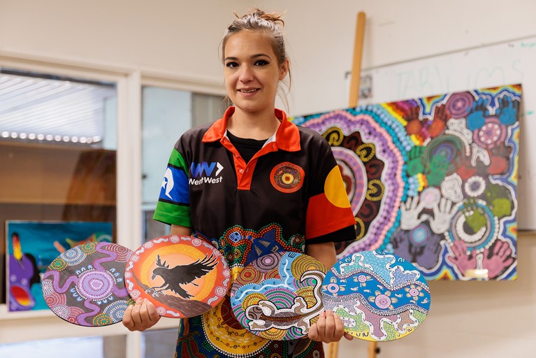 Tereesa with four of her artworks that were displayed at the 2022 Vivid Festival Sydney at Baabayn Aboriginal Corporation in western Sydney. Photo: Richard Wainwright/Caritas Australia