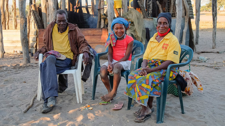 Anatercia sits with her grandfather and grandmother outside their home in Mozambique. Photo credit: Emidio Josine/Caritas Australia.