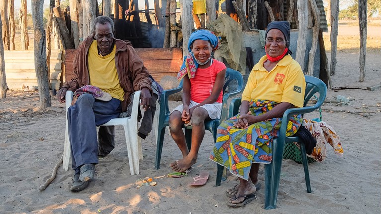 Anatercia sits with her grandfather and grandmother outside their home in Mozambique. Photo credit: Emidio Josine/Caritas Australia.
