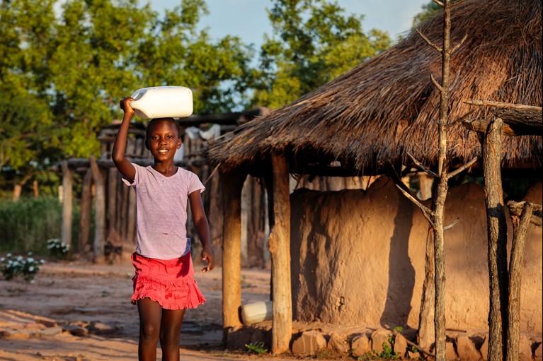 Thandolwayo (9) outside her home holding a 5 litre water container she uses to collect water in Msuna Hills, Zimbabwe. In June 2017, Caritas Hwange, a Caritas Australia partner, installed a solar powered piped water system in Msuna Hills bringing fresh clean drinking water to the population for the first time. Photo credit: Richard Wainwright/Caritas Australia.