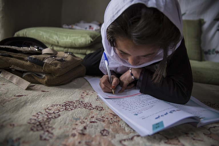 A young girl writes in a notebook in Afghanistan. Photo credit: CRS.