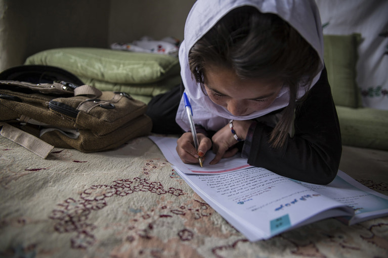 A young girl writes in a notebook in Afghanistan. Photo credit: CRS.