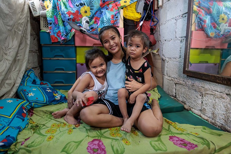 Ronita (22) smiles as she holds her sons, Egzy Grey (3) and Clark (5), in their small home in Quezon City, Philippines. Photo: Richard Wainwright/Caritas Australia 