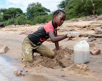 Thandolwayo (9) demonstrates how she used to collect dirty water from the Gweyi river before a new water pipe was installed in Zimbabwe. Credit: Richard Wainwright/Caritas Australia